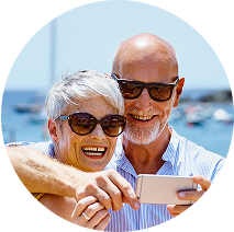 An older couple standing outside near the ocean while they look at a phone