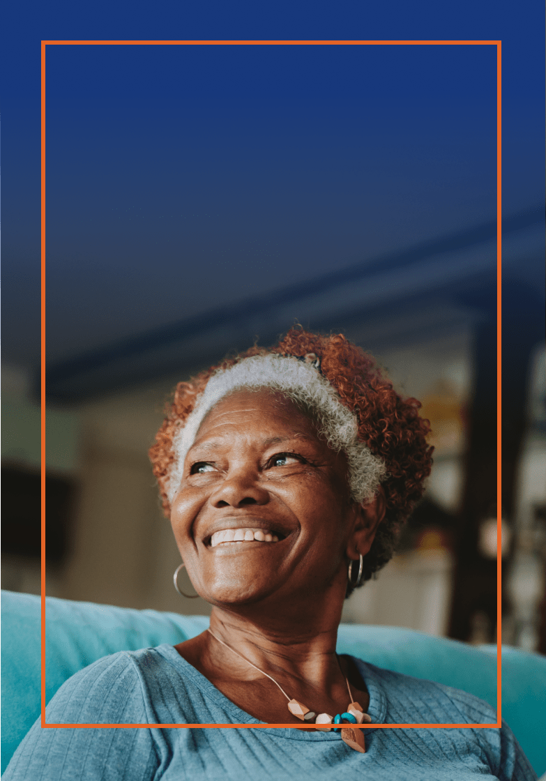 Older woman with graying hair smiling while she is sitting on a couch
