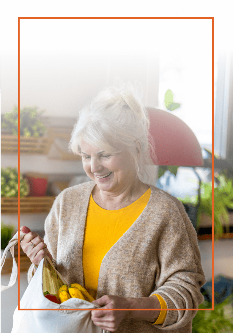 Older woman smiling with a bag of groceries