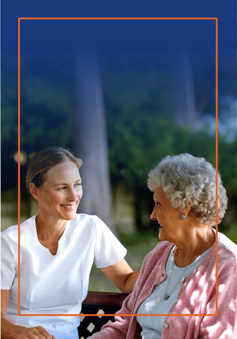 A woman sitting next to their elderly mother on a park bench, both are smiling