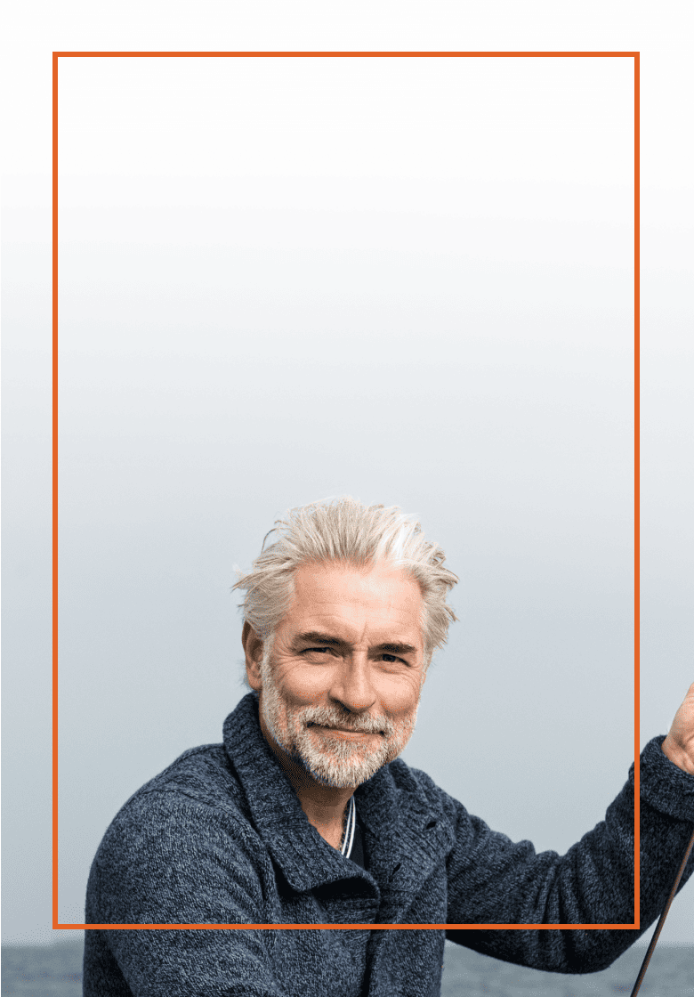 Older man with white hair standing in front of the ocean