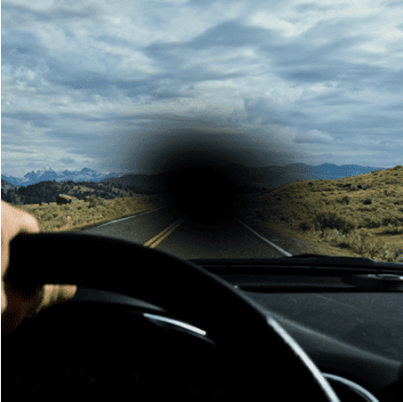 Point of view photo of someone driving a car down a scenic road, but a black dot has formed in the center of the image