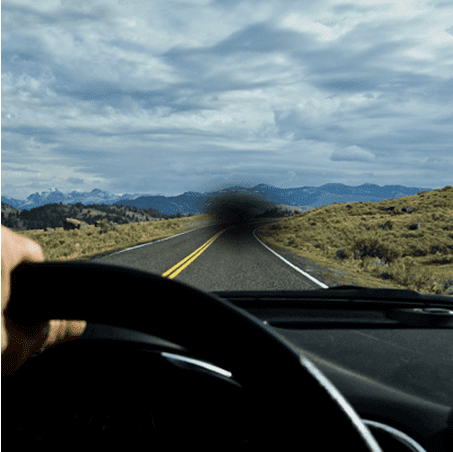Point of view photo of someone driving a car down a scenic road, but a small black dot has formed in the center of the image