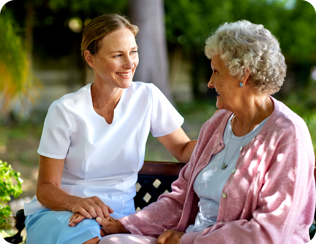 Older woman and younger woman sitting outside, while smiling at each other