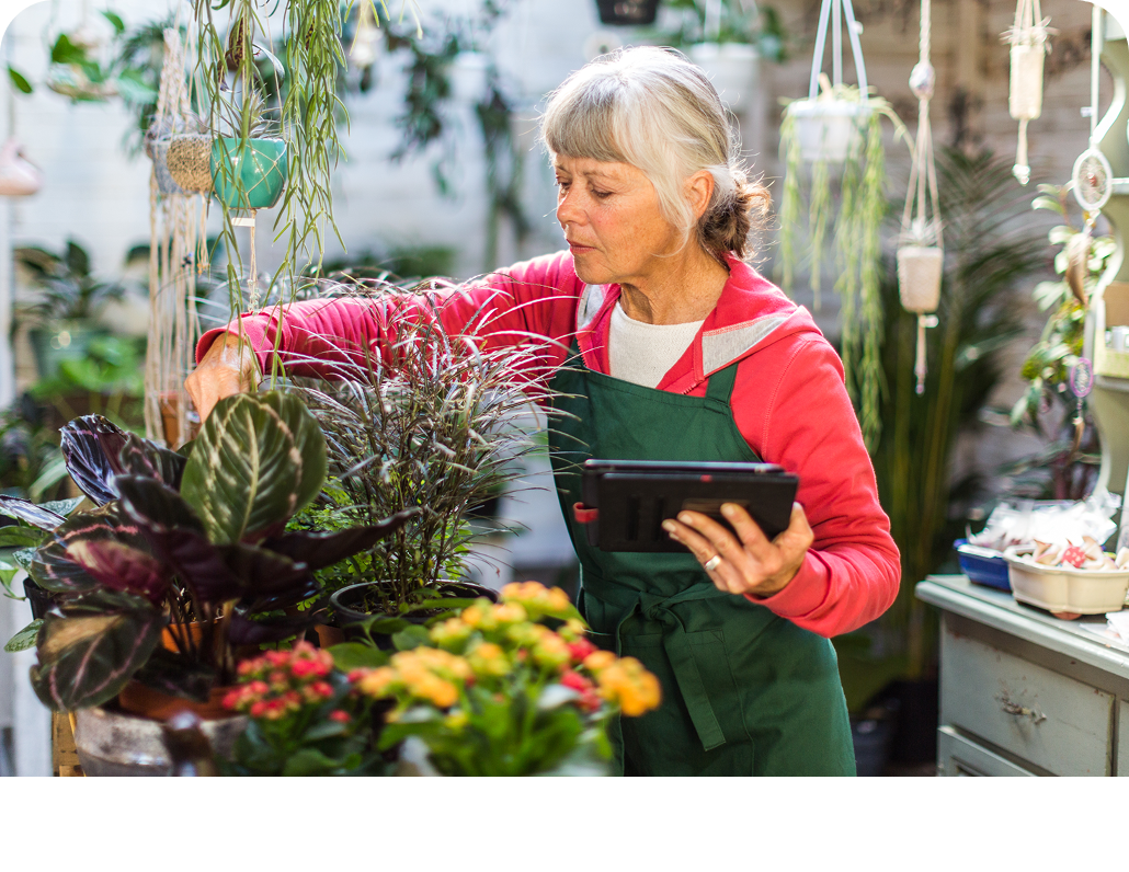 Elderly woman with a tablet in hand tending to plants